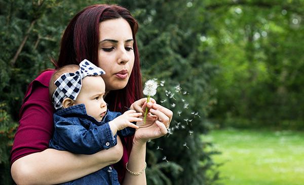 mother holding her baby and blowing a dandelion